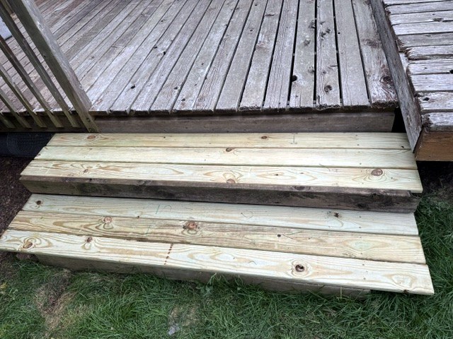 Two new pressure-treated wood steps built at the edge of a backyard deck