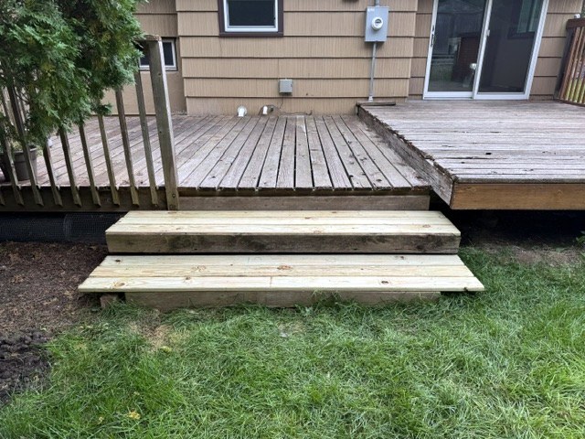 New wood steps leading up to a backyard deck, seen from the lawn