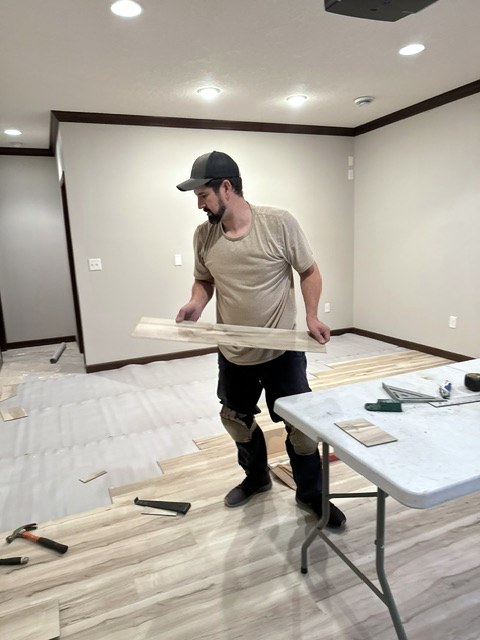 Jesse from Morehouse Repairs installing luxury vinyl plank flooring in a finished basement