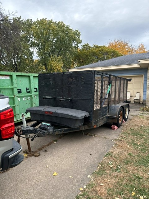 Morehouse Repairs utility trailer hitched to a pickup in a driveway beside a dumpster