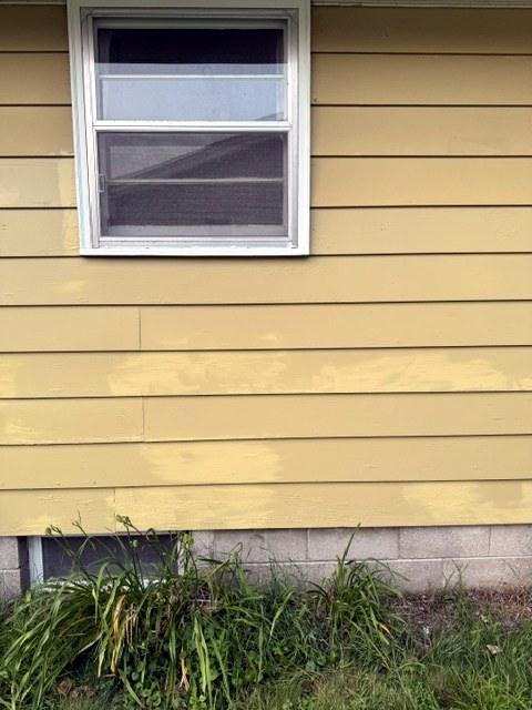 Tan lap siding below a window with bare spots spot-primed before painting