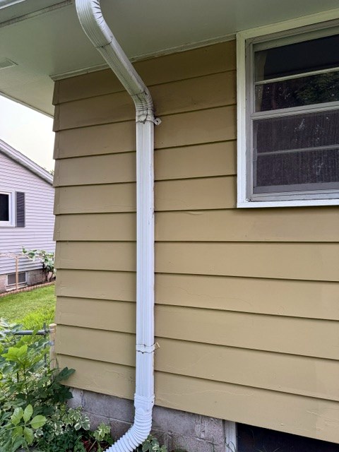 Freshly painted tan siding beside a white downspout and window